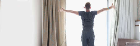 Successful man stands in bedroom near bright windowの写真素材
