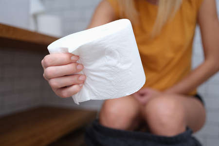 Woman sits on toilet and holds toilet paper in handsの写真素材