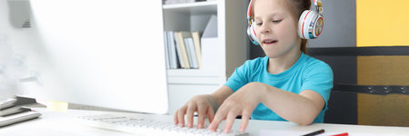 Girl in headphones sits at computer monitor and types on keyboard