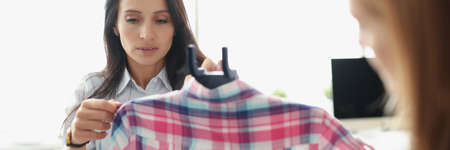 Women seamstresses taking measurements of shirts with centimeter tape and ironing with steamerの写真素材