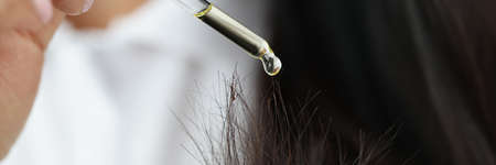 Woman dripping yellow oil from pipette on split ends of hair closeup