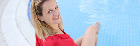 Young smiling woman is sitting on edge of pool