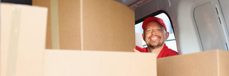Smiling male courier pulls out cardboard box from carの写真素材