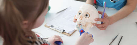 Little girl pulling out tooth with toy medical instruments on astronomical skull at dentist appointment closeupの写真素材