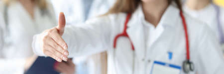 Woman doctor giving hand for handshake on background of colleagues in clinic closeupの写真素材