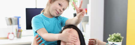 Little girl closing eyes of smiling mother at homeの写真素材