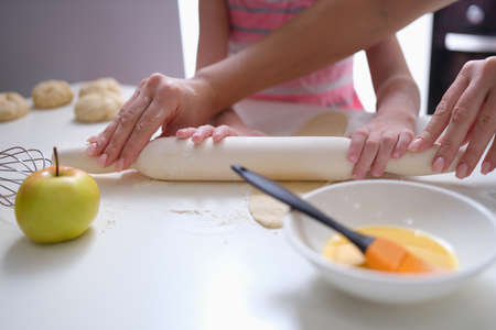Mother and daughter rolling out flour dough at table closeupの写真素材