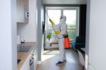 Man in protective suit treating with disinfectant flatの写真素材