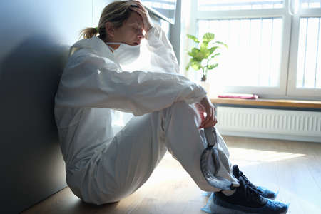 Tired doctor in protective antiplague suit sitting on corridor of clinicの写真素材