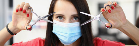 Portrait of female hairdresser in protective medical mask holding scissorsの写真素材