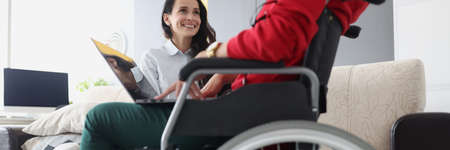 Woman in wheelchair with laptop communicates with friendの写真素材