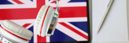 Tablet with image of British flag with headphones and notebook with pen lie on tableの写真素材