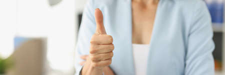 Businesswoman in suit holds thumbs up in officeの写真素材