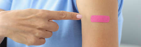 Pink plaster on woman shoulder after shot of vaccineの写真素材