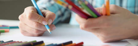 Female hands hold multi-colored pencils and sheet of paper lies on tableの写真素材