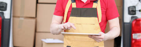 Cute caucasian postman in suit and cap checks mailboxes with tablet device in his handsの写真素材