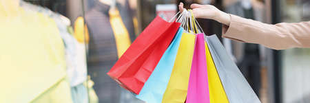 Multicolored paper bags on female hands on background of shopping mallの写真素材
