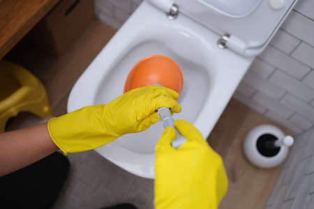 Person in yellow gloves and plunger cleans toilet closeupの写真素材