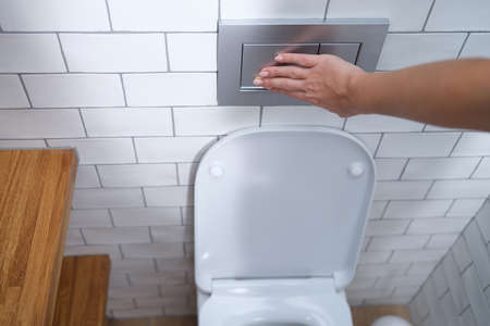 Female hand presses flush button in toilet closeupの写真素材