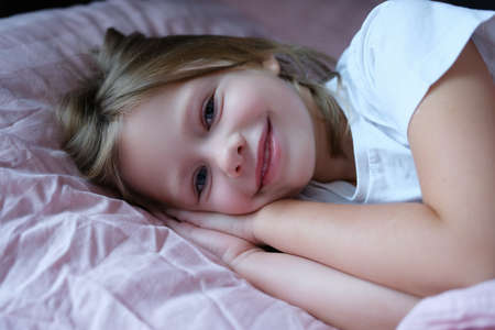 Portrait of little beautiful smiling girl lying on pillowの写真素材