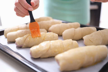 Woman hand is brushing egg yolk onto sweet flour rollsの写真素材