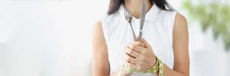 Woman with hands tied with measuring tape holding fork and knife closeupの写真素材