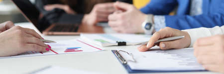 Group of business people are sitting at table with laptop and documents with charts closeup