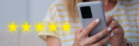 Woman holding mobile phone in her hands and giving five star rating for quality of services closeupの写真素材