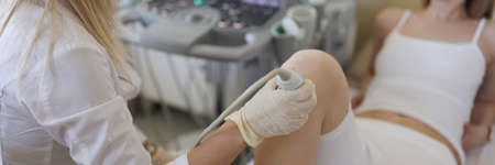 Doctor doing ultrasound of knee joint to young woman in clinic closeupの写真素材