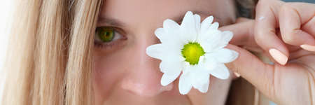 Portrait of beautiful young woman with green eyes closes one eye with flowerの写真素材