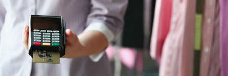 Clothes seller holding pos terminal in his hands in shop closeup