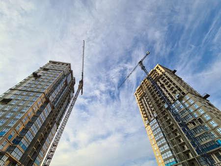 Cranes standing near multi-storey buildings under construction against background of blue sky bottom viewの写真素材