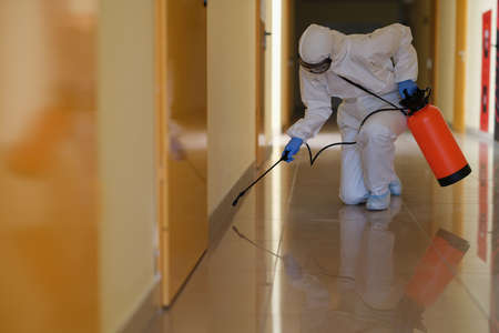 Specialist in protective suit and mask disinfects corridors closeup
