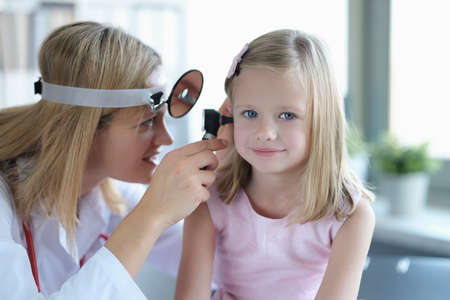 ENT doctor looks at little girls ears with otoscope closeupの写真素材