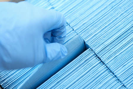 Nurse wearing protective rubber gloves pulling out sterile blue medical napkin closeup