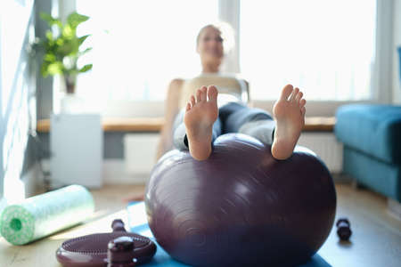 Woman performs sports exercises on ball at home closeupの写真素材