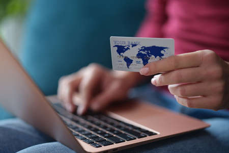 Woman holds bank card in hands and enters data into laptop closeupの写真素材