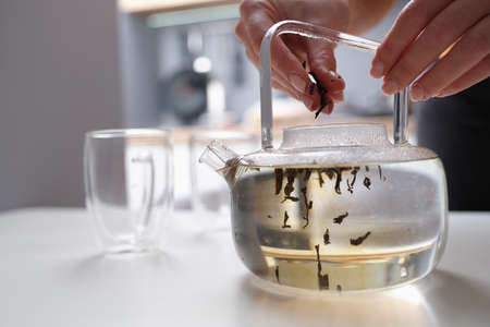 Woman falls asleep tea leaves in transparent glass teapot with hot waterの写真素材
