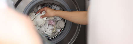 Female hand pulling out clean linen from washing machine closeupの写真素材