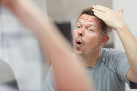 Unshaven man looks in the mirror and straightens his hairの写真素材