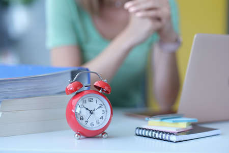 Woman sits at workplace next to alarm clock at ten in morningの写真素材