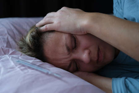 A woman lies with her eyes closed and holds her head with her handsの写真素材