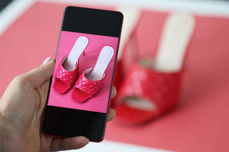 Woman photographing red elegant high heeled sandals on mobile phone closeupの写真素材