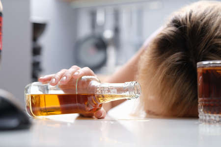 Woman sleeping at table with bottle of alcohol in her hands closeupの写真素材