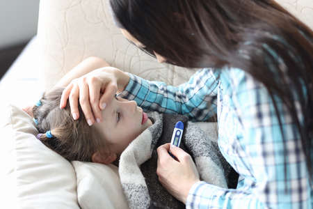 A caring mother touches the forehead of a sick girl