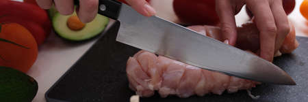 Woman hand cuts meat fillet with knife on board next to garlicの写真素材