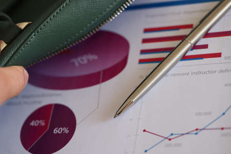 Man putting ballpoint pen and documents with charts in leather bag closeupの写真素材