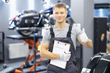 Portrait of young car mechanic holding clipboard and thumb up in car service