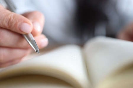 Womans hand holding a pen near notepad, close-upの写真素材