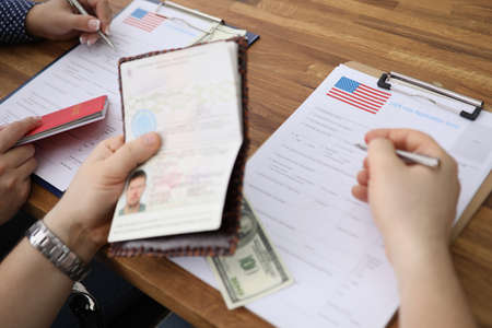People filling visa application forms with personal passports at embassyの写真素材